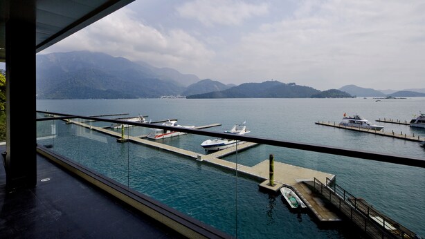 A marina with boats docked, a clear view of mountains, and a glass railing overlooking the water.