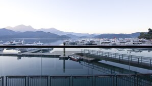 A marina with boats docked, calm water, and mountains in the background.