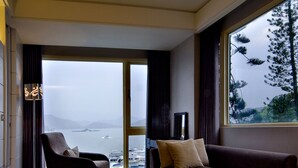 A modern living room with a sofa, armchair, and a large window offering a view of the sea.