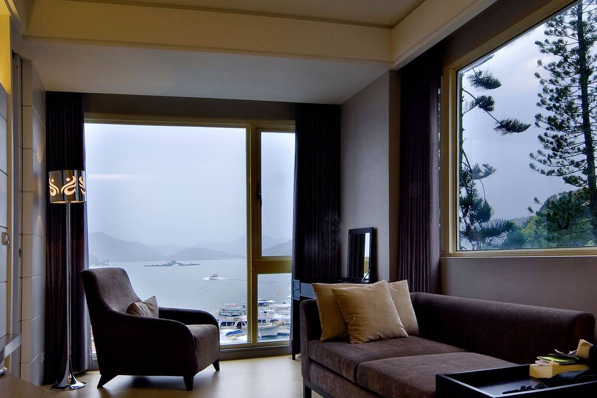 Ein modernes Wohnzimmer mit einer Couch, einem Sessel und einem großen Fenster mit Meerblick.