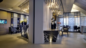 A modern lobby with a marble reception desk, seating area, and large windows.