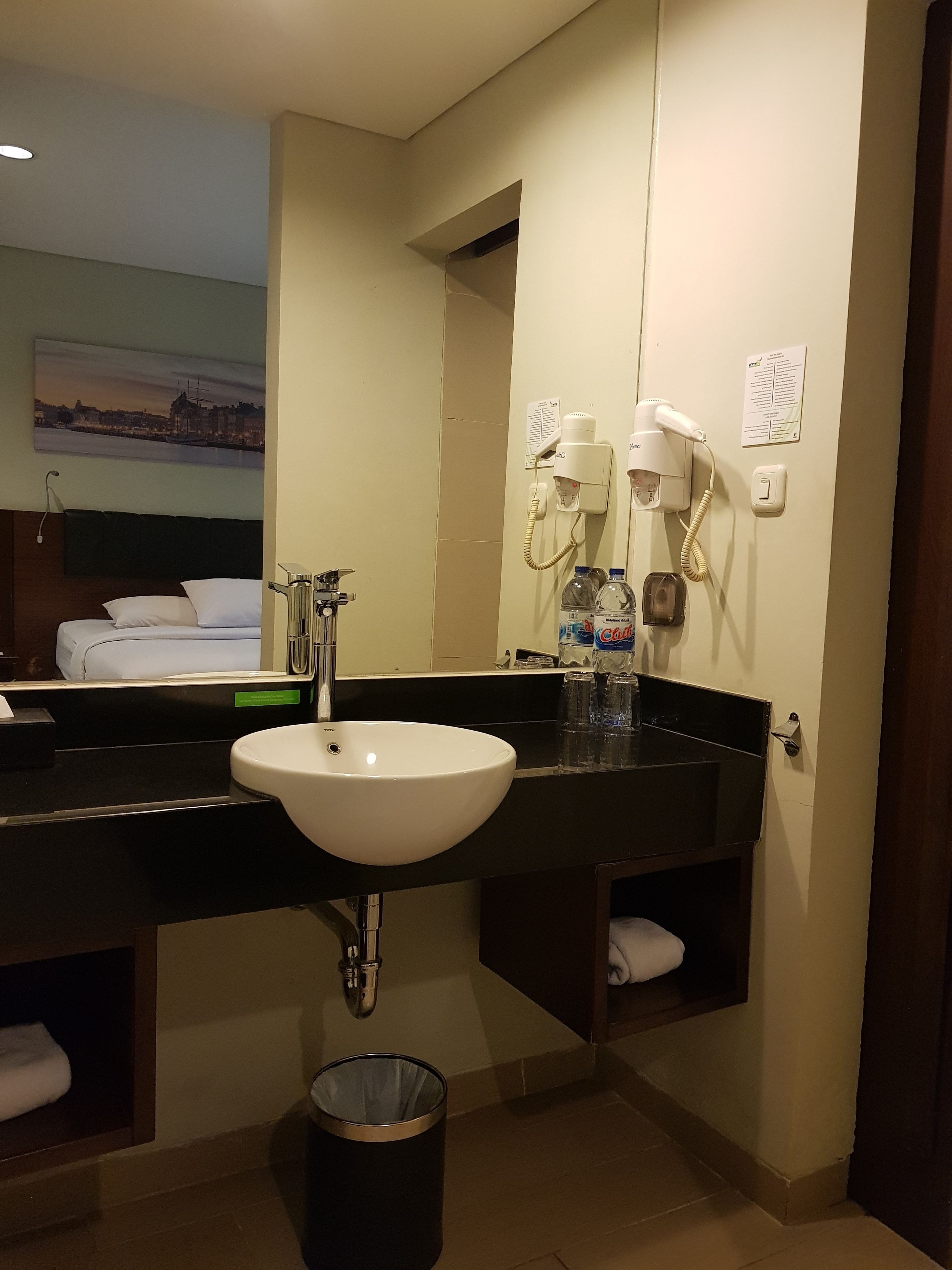 A hotel bathroom with a large sink, a mirror, a hairdryer, and a towel rack.