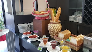 A buffet setup with bread, pastries, and various condiments.