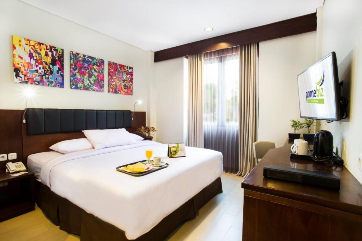 Una habitación de hotel con cama, escritorio, televisión y una obra de arte en la pared.
