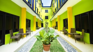 A hotel corridor with bright yellow and green walls, multiple windows, and outdoor seating areas with chairs and tables.