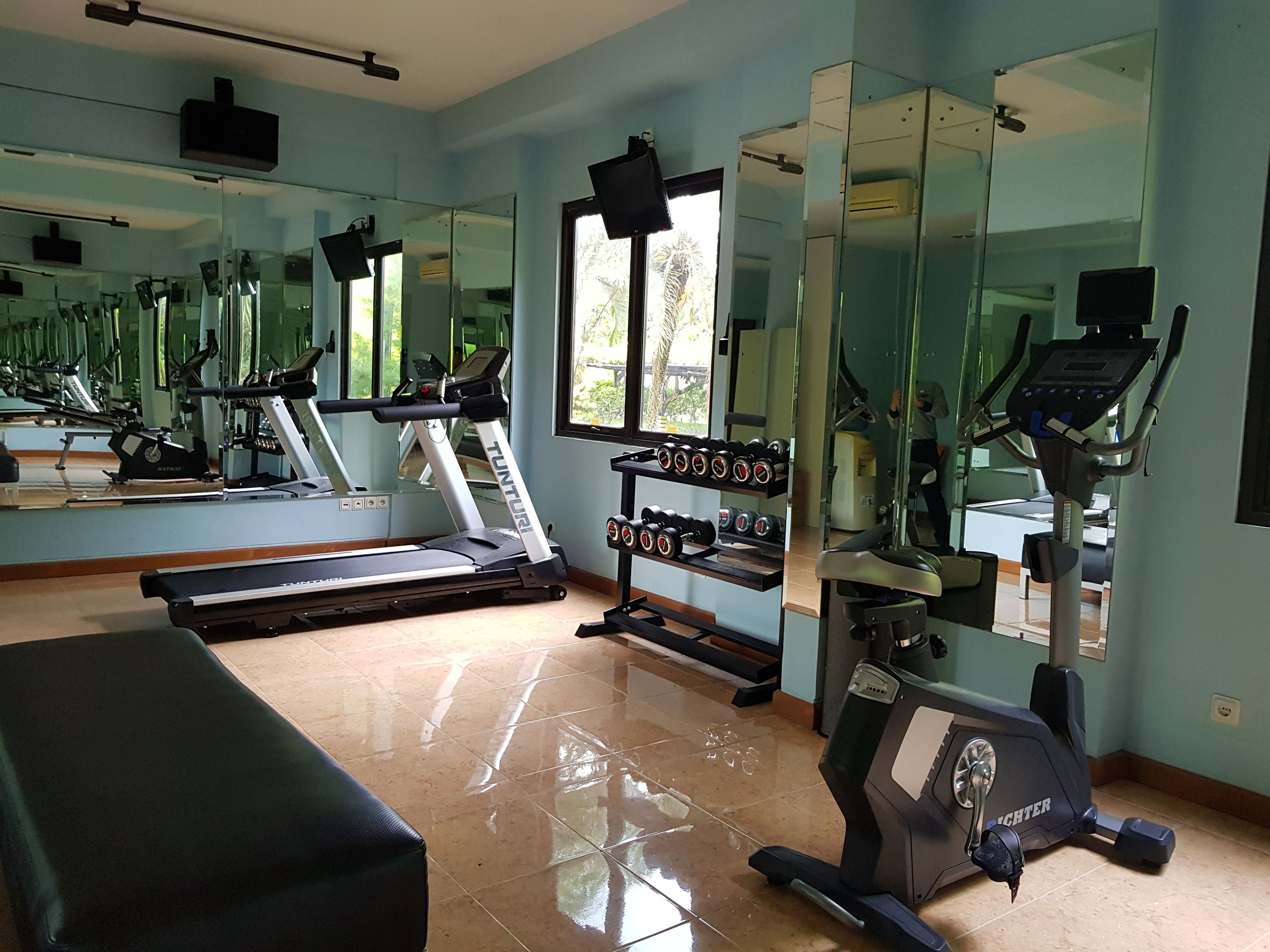 Un gimnasio con equipo de ejercicio, cinta de correr y pared espejada.