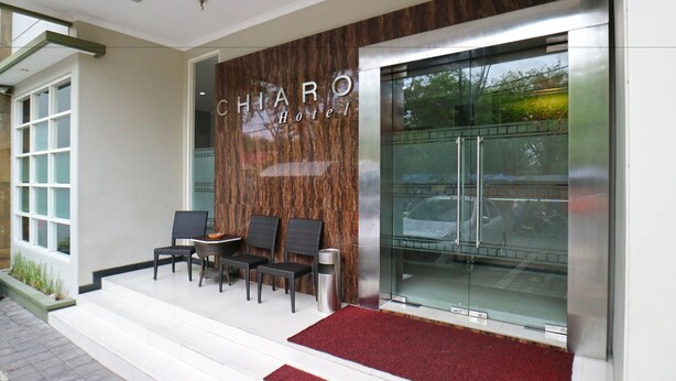 The exterior of the Chiaro Hotel with a modern facade, a glass entrance, and a seating area with chairs and a small table. - Chiaro Hotel Syariah (Sidoarjo)