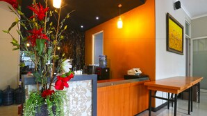 A reception area with a wooden counter, a vase with red flowers, and a water dispenser. - Chiaro Hotel Syariah (Sidoarjo)
