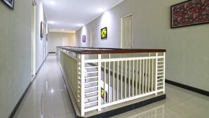 A corridor with a white railing, tiled floor, and framed artwork on the walls. - Chiaro Hotel Syariah (Sidoarjo)