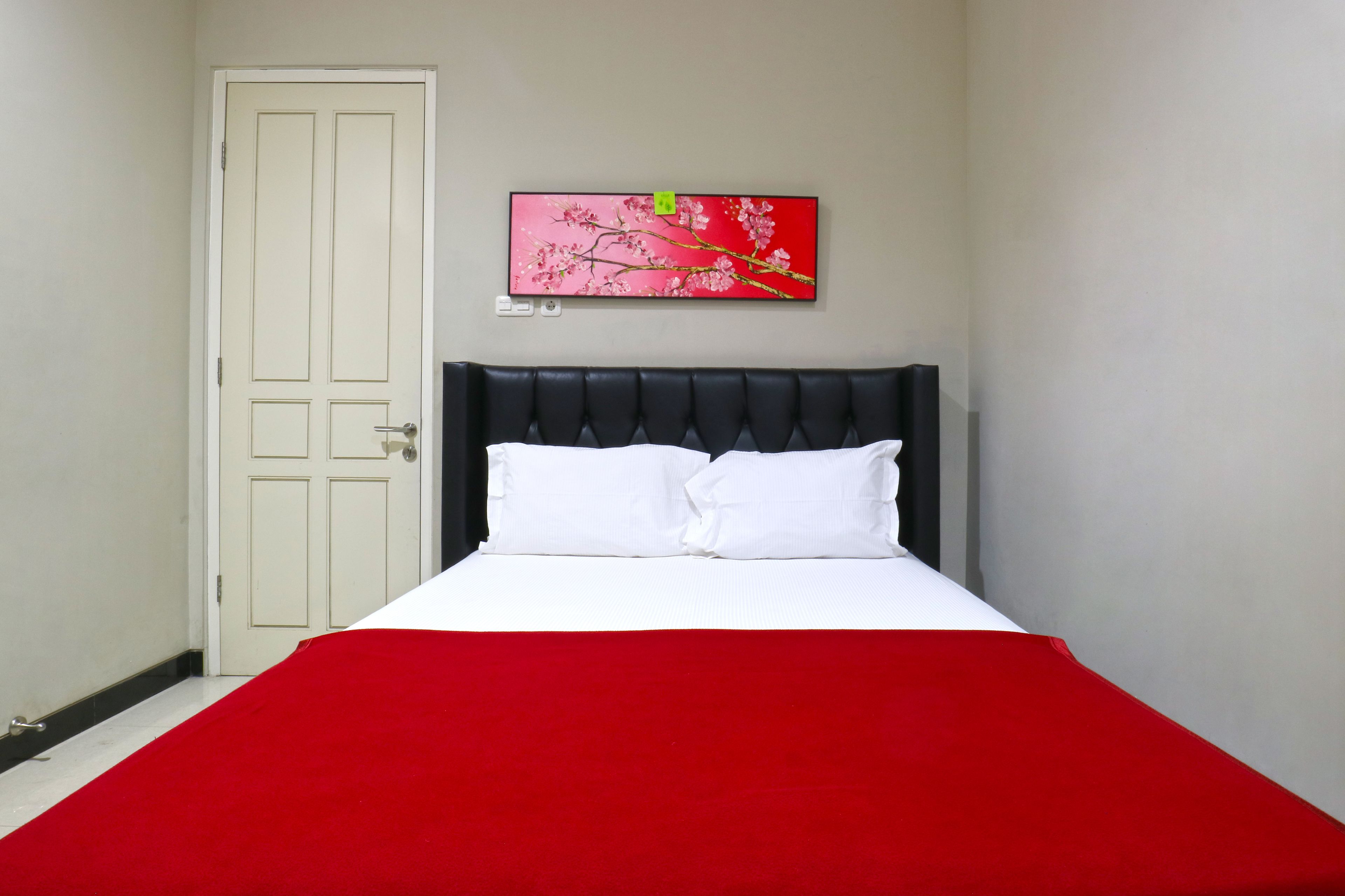 Une pièce avec un lit, une porte blanche et un mur rouge.