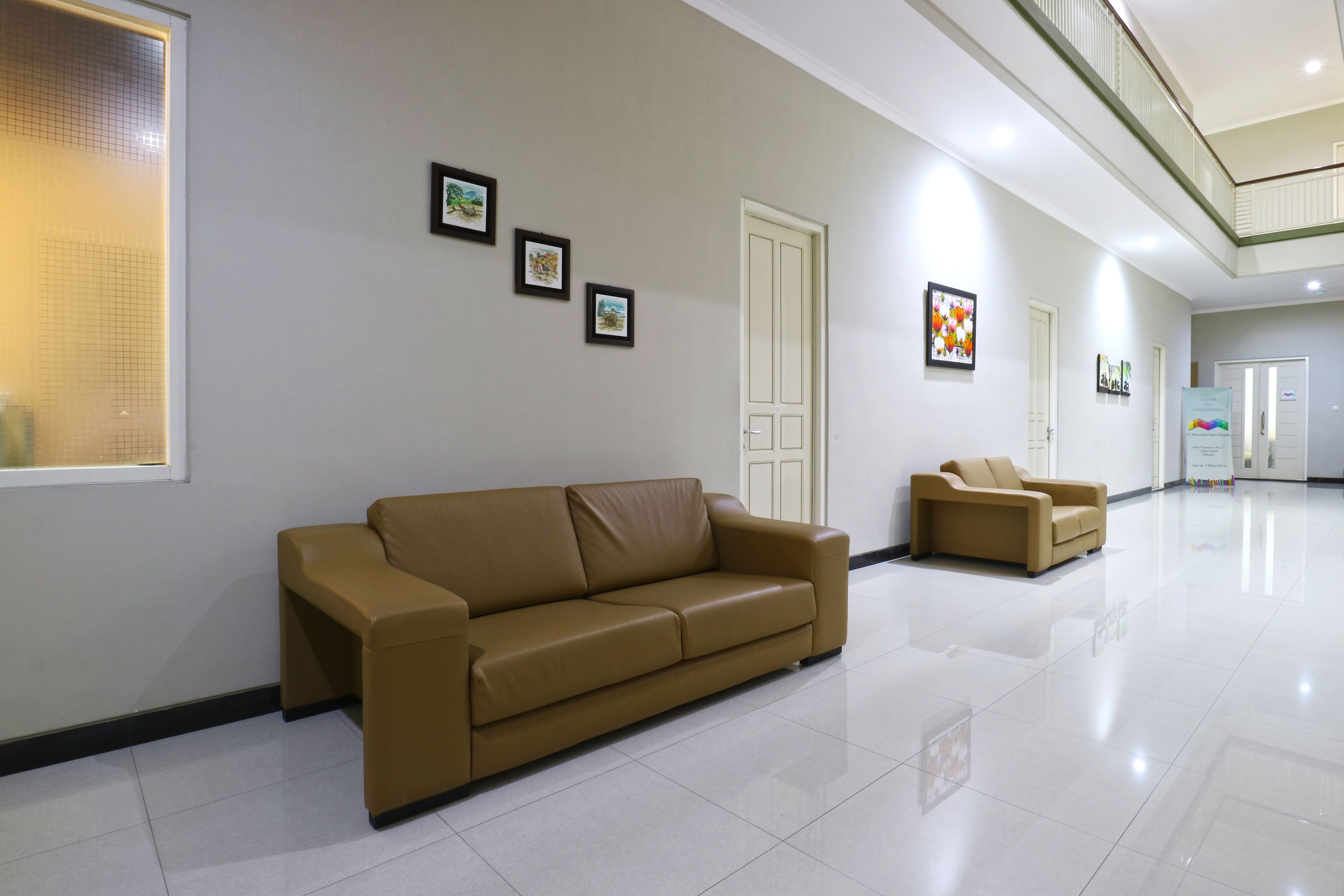 A spacious lobby with a beige leather sofa and armchair, a large window, and framed artwork on the walls.
