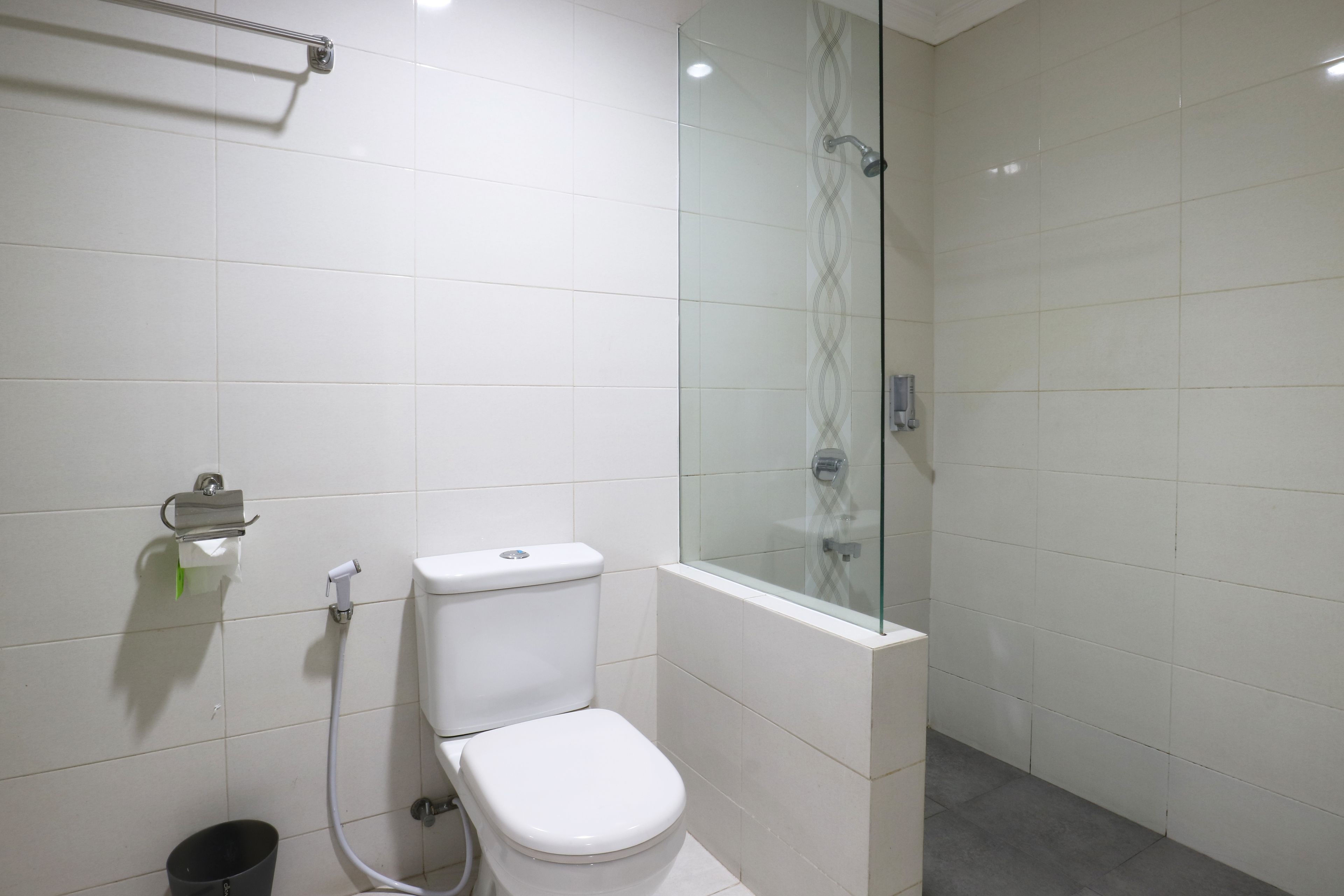 Een moderne badkamer met toilet, een douchecabine van glas en een handdoekhouder.