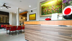 A reception area with a wooden reception desk, red chairs, and a large floral painting on the wall. - Chiaro Hotel Syariah (Sidoarjo)