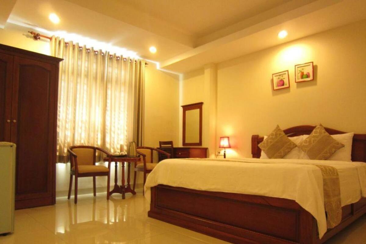 A hotel room with a large bed, a desk, a chair, a mirror, and a lamp.