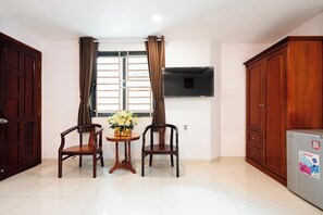 A room with a TV mounted on the wall, two wooden chairs, a small table with a vase of flowers, and a cabinet.
