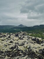 A rocky terrain with a mountain in the distance under a cloudy sky.
