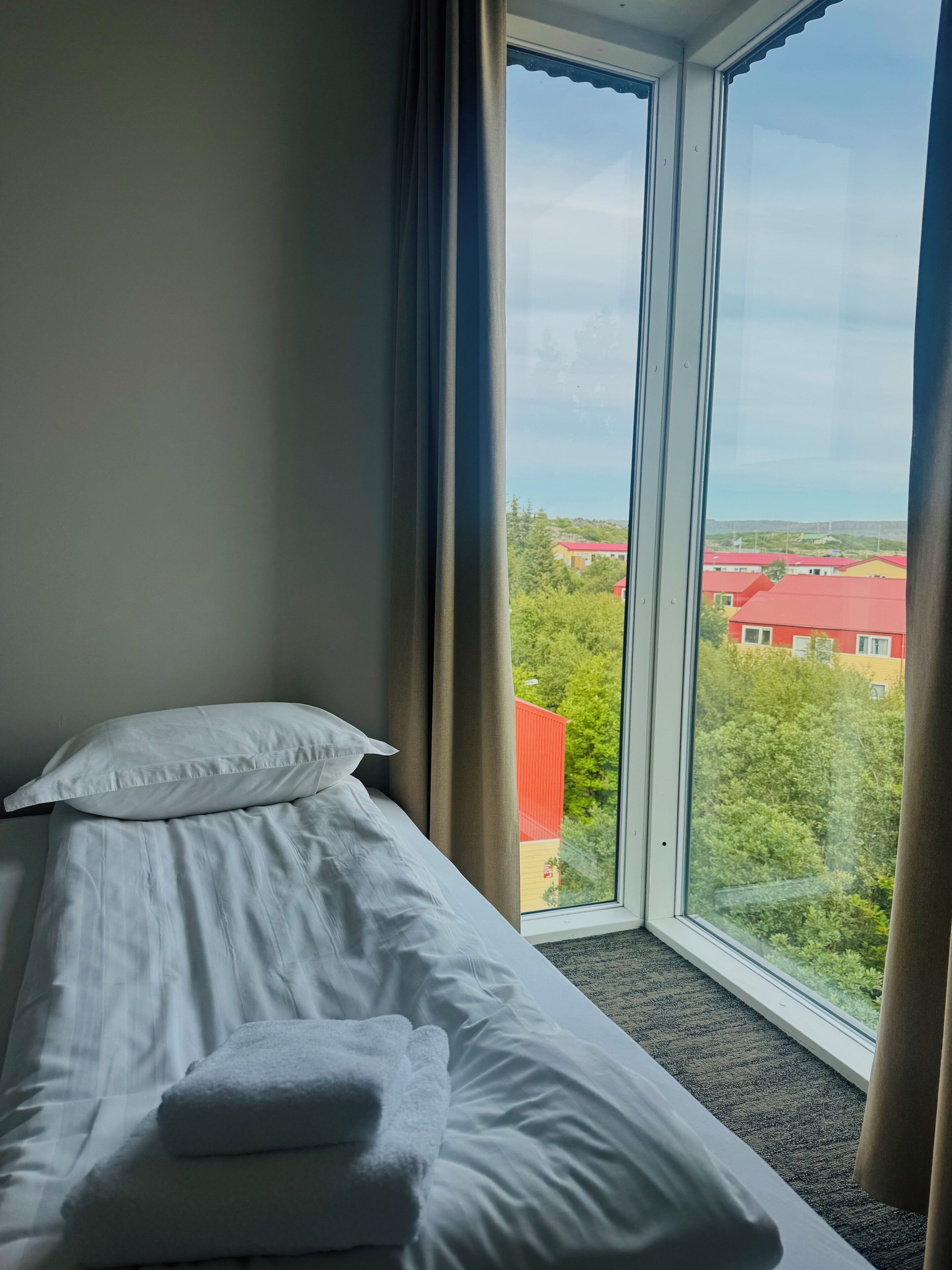 Habitación de hotel con cama, ventana y vista a edificios.