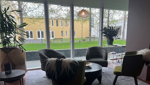 A modern interior with large windows, wicker chairs, a round table, and a potted plant. - Hotel Bifrost (Borgarbyggd)