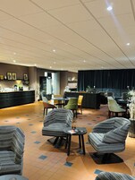 Un vestíbulo de hotel con mostrador de recepción, zona de estar con sillones estampados y suelo de baldosas.