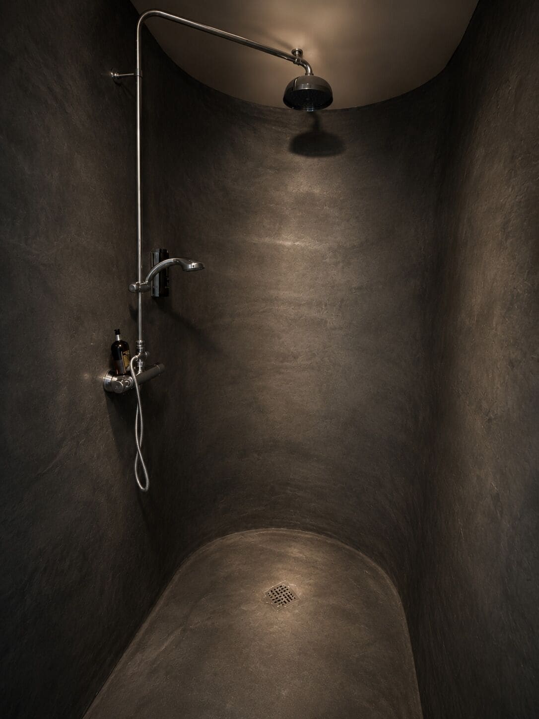 A dark, minimalist shower with a handheld showerhead and a wall-mounted faucet.