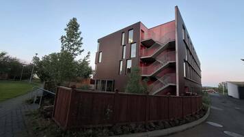 A multi-story building with balconies, a wooden fence, and a paved driveway.