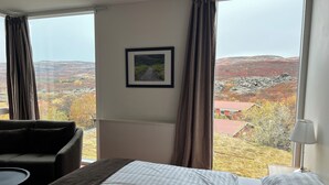 A hotel room with a large bed, a sofa, and a view of a mountainous landscape. - Hotel Bifrost (Borgarbyggd)