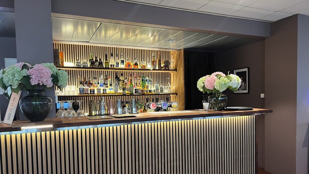 A modern bar area with a wooden slat design, a variety of liquor bottles, and two vases with flowers. - Hotel Bifrost (Borgarbyggd)