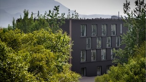 A modern building with a dark facade, surrounded by lush greenery and mountains in the background. - Hotel Bifrost (Borgarbyggd)
