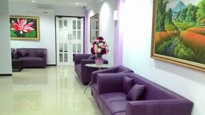 Un'area reception con divani viola, un vaso di fiori e un quadro appeso al muro.