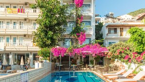 A hotel pool area with lounge chairs, a clear pool, and a building with balconies. - Hotel Koza (Kas)