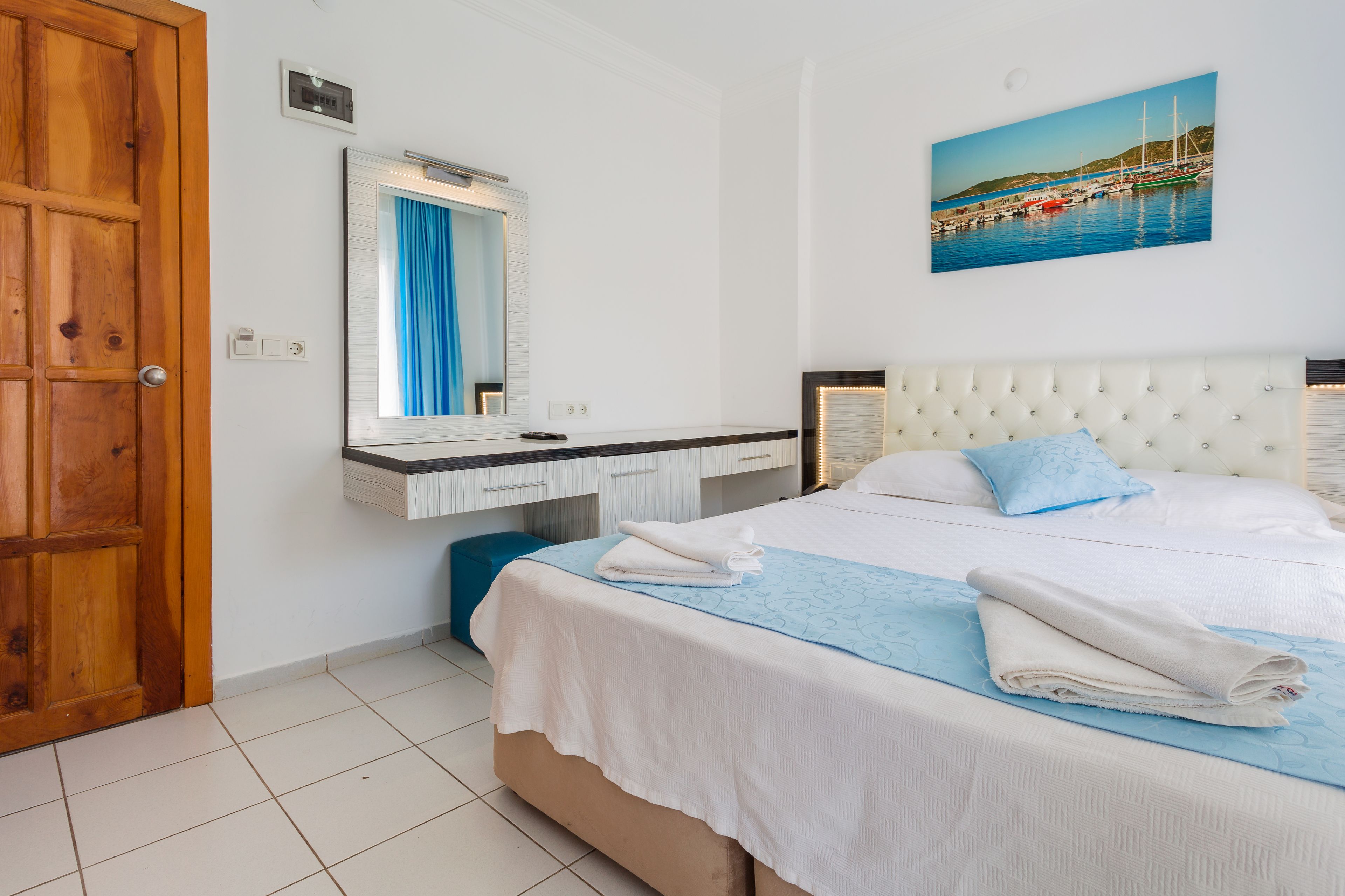 Una habitación de hotel con una cama, una puerta de madera, un baño con espejo y un cuadro en la pared.