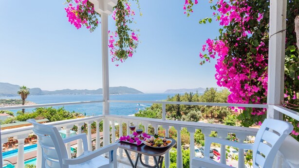 A balcony with white chairs, a table with fruit and drinks, and a view of the sea and mountains. - Hotel Koza (Kas)