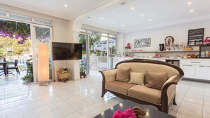 A spacious living area with a sofa, a coffee table with flowers, a TV, and a kitchen area with a chalkboard menu. - Hotel Koza (Kas)