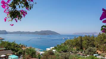 A coastal view with a clear blue sea, boats, and a mountainous backdrop.