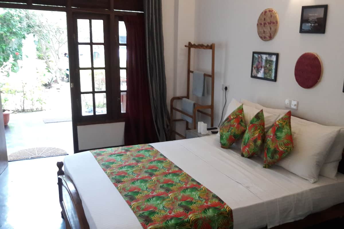 A bedroom with a bed, pillows, a wooden chair, a small table, and a wall with framed pictures.