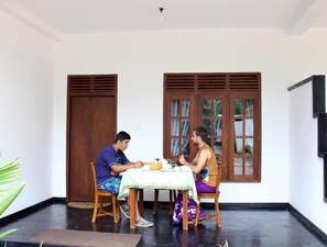 Una habitación con una mesa de comedor, dos sillas, una ventana con contraventanas de madera y una puerta.