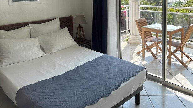 Une chambre d’hôtel comprenant un lit, une table de chevet, une lampe, une fenêtre avec des rideaux et un balcon avec une table et des chaises.