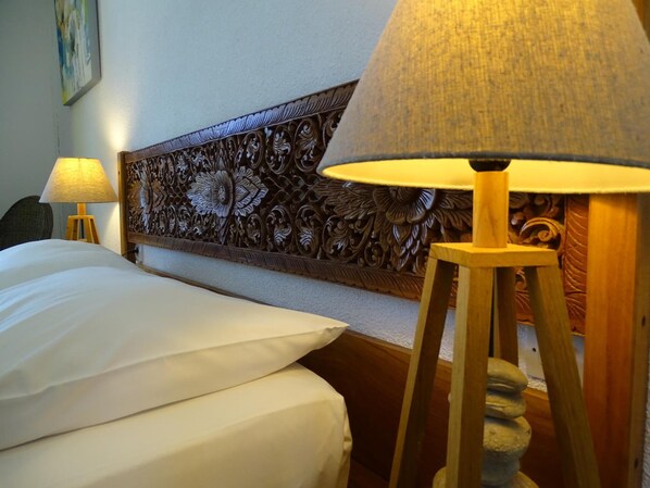 A hotel room with a neatly made bed, a wooden headboard with intricate carvings, and a lamp on a wooden stand. - Résidence Le Phoenix (Saint-Pierre)