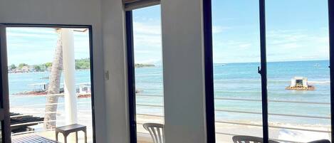 Ein Zimmer mit großen Fenstern, die Blick auf einen Strand, eine Palme und das Meer bieten.