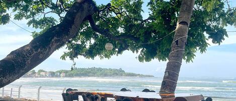 A seaside table and chairs under a tree, overlooking the ocean.