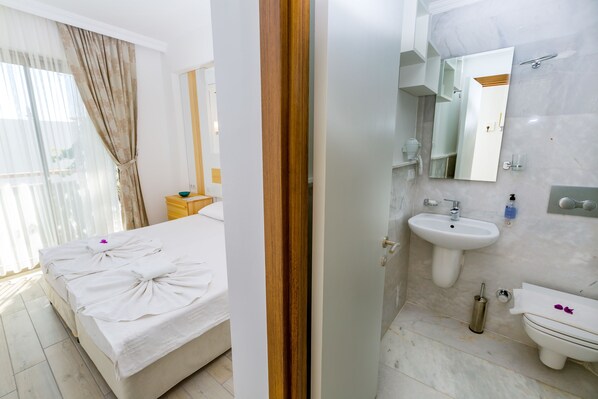 A bedroom with a bed, a bathroom with a sink, mirror, and toilet. - Defne Hotel (Kas)