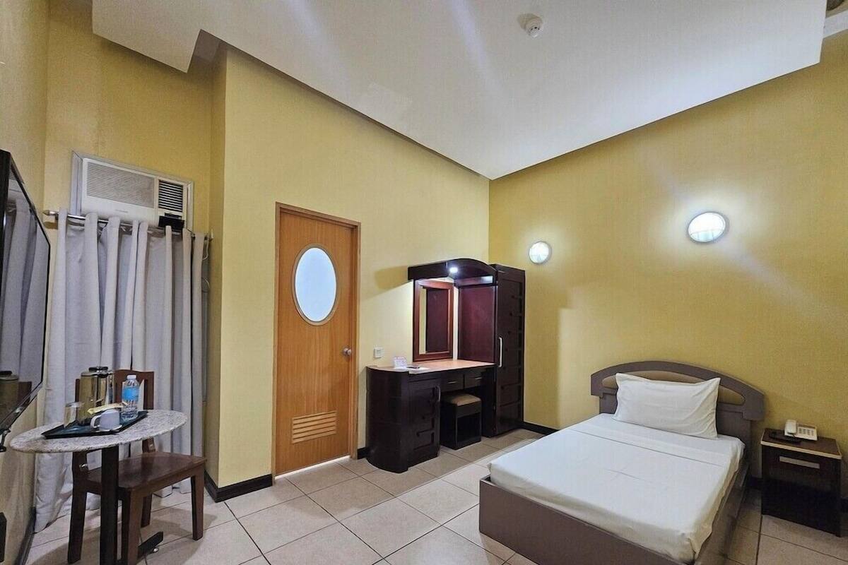 Una habitación de hotel con cama, escritorio con espejo, una mesita con silla y ventana con cortinas.