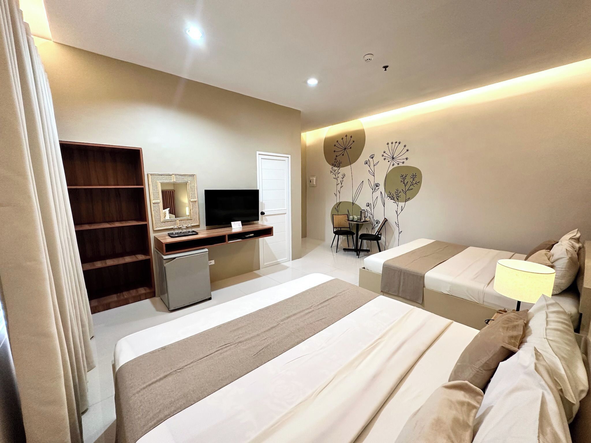 A hotel room with two beds, a desk with a computer, a small fridge, a TV, and a wardrobe.