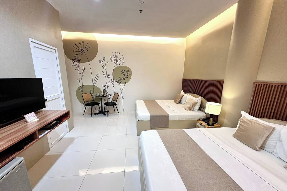 Habitación de hotel con dos camas, televisión, mesa de comedor con sillas y un adorno en la pared.