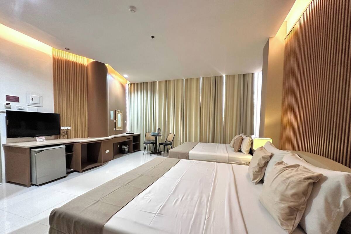 Habitación de hotel con una cama grande, un escritorio con televisión y una zona de estar con mesa y sillas.