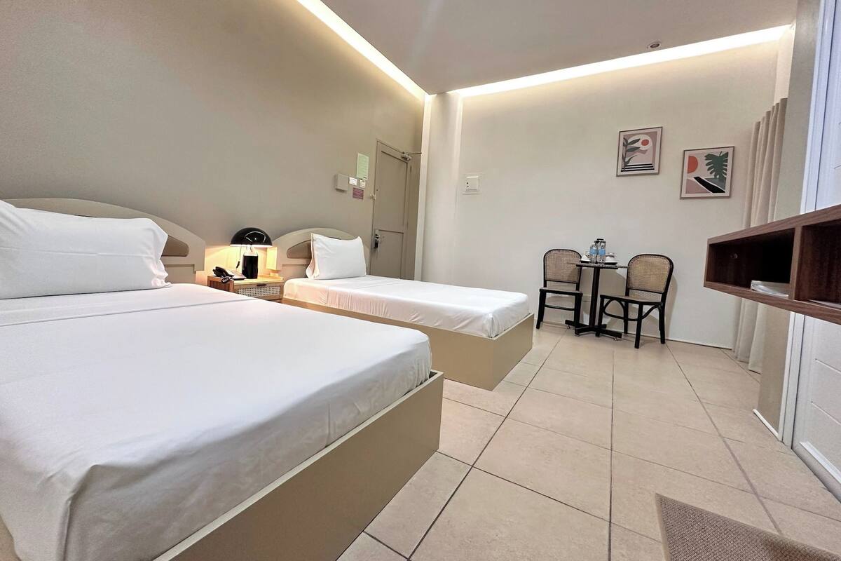 Habitación de hotel con dos camas, un escritorio con sillas y una mesita con una botella de agua.