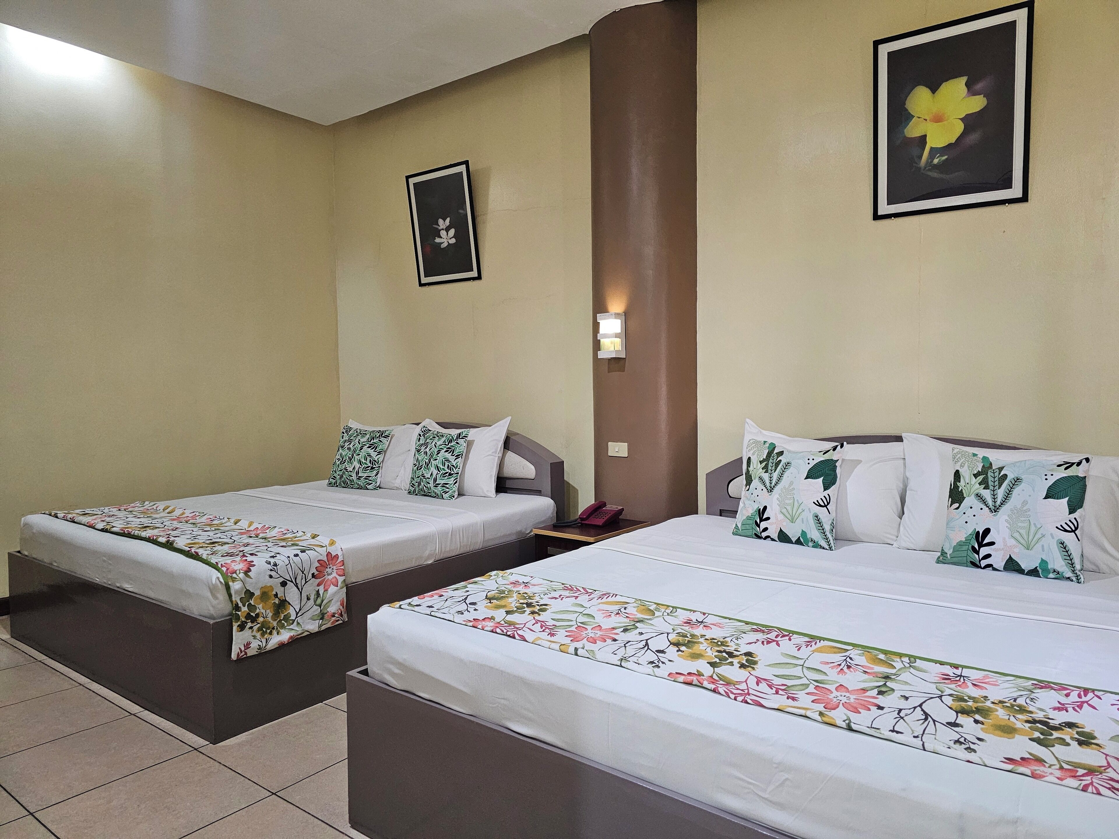 Two single beds with floral bedspreads, a nightstand with a phone, and a wall-mounted light fixture.