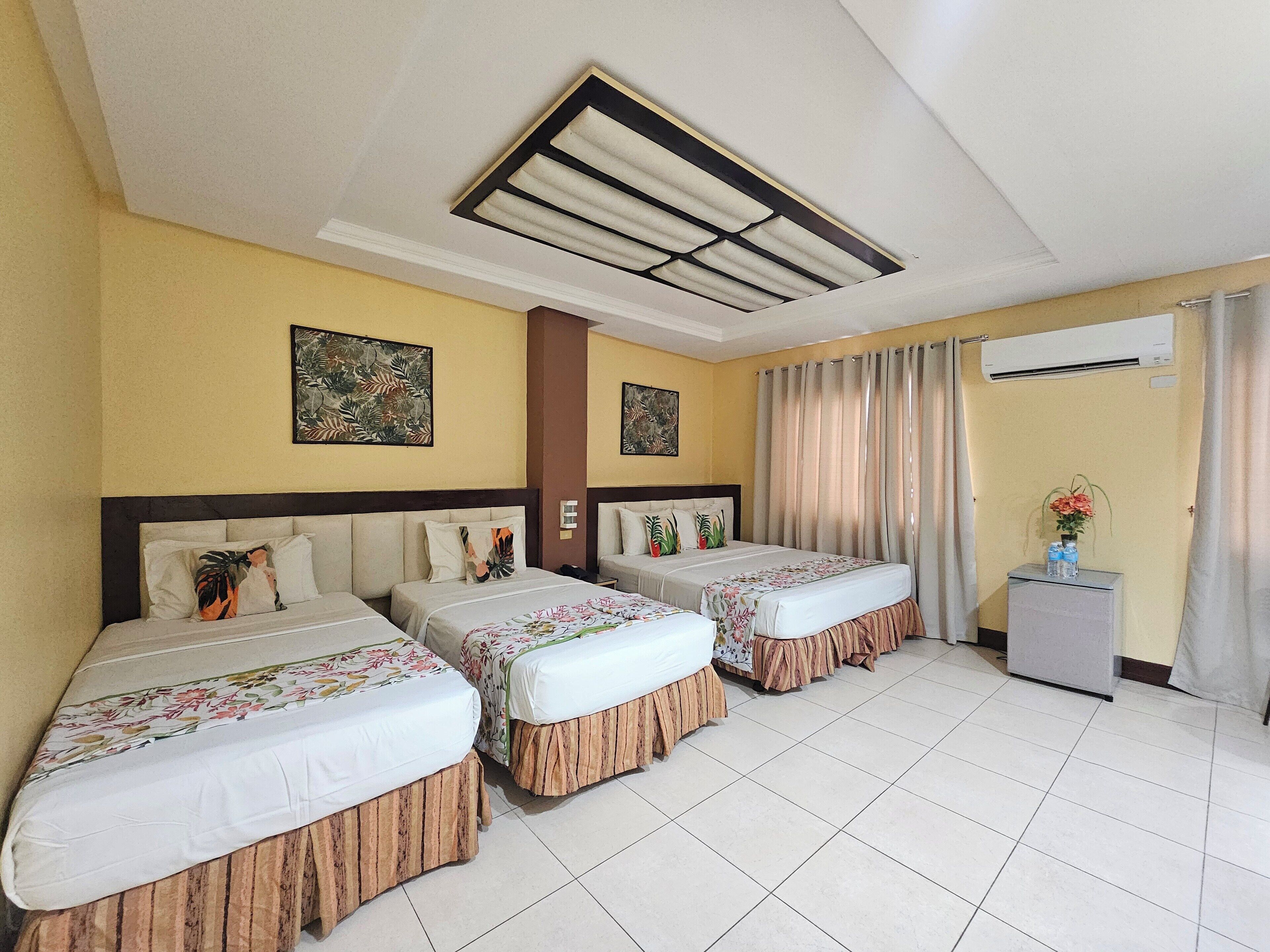 Habitación de hotel con dos camas, un ventilador de techo, un equipo de aire acondicionado y una mesita con un florero.