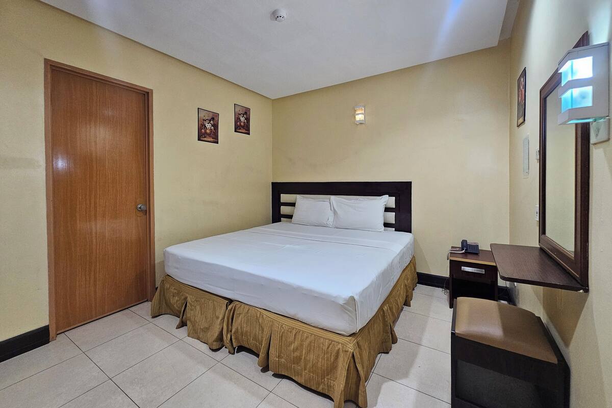 Habitación de hotel con cama, escritorio, silla, puerta y teléfono en la pared.