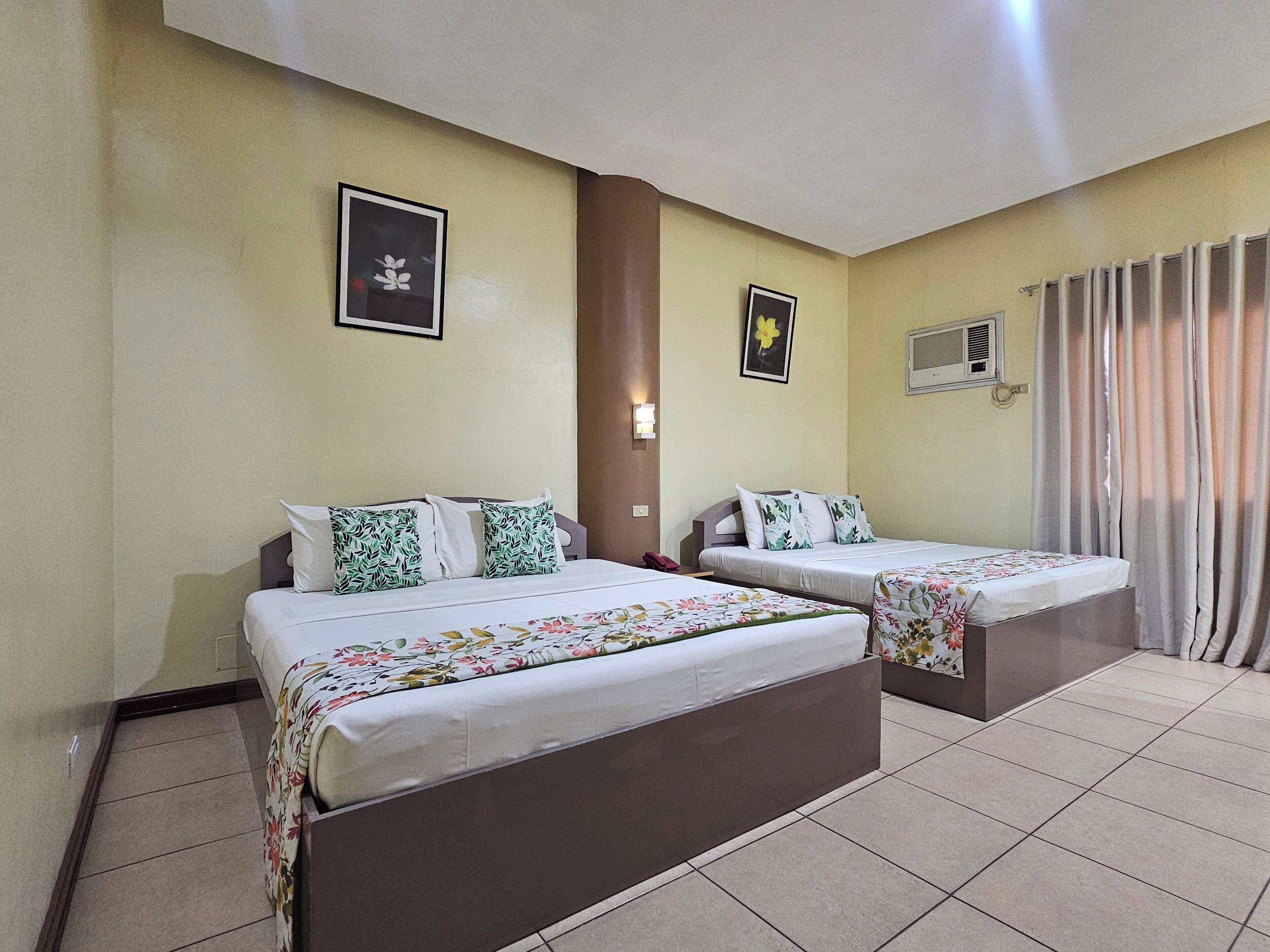 A hotel room with two beds, a wall-mounted air conditioner, and a window with curtains.